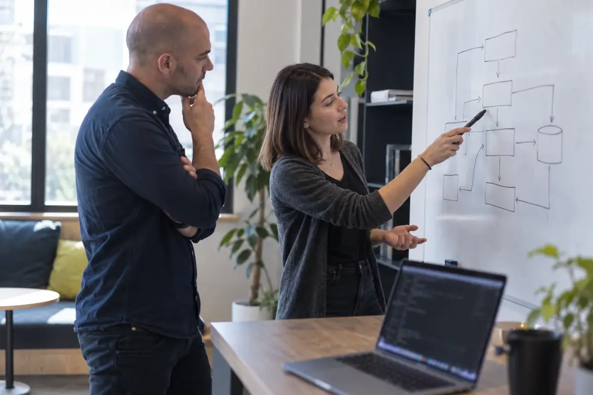 Ingénieure présentant un schéma d'architecture technique sur un tableau blanc à un collègue