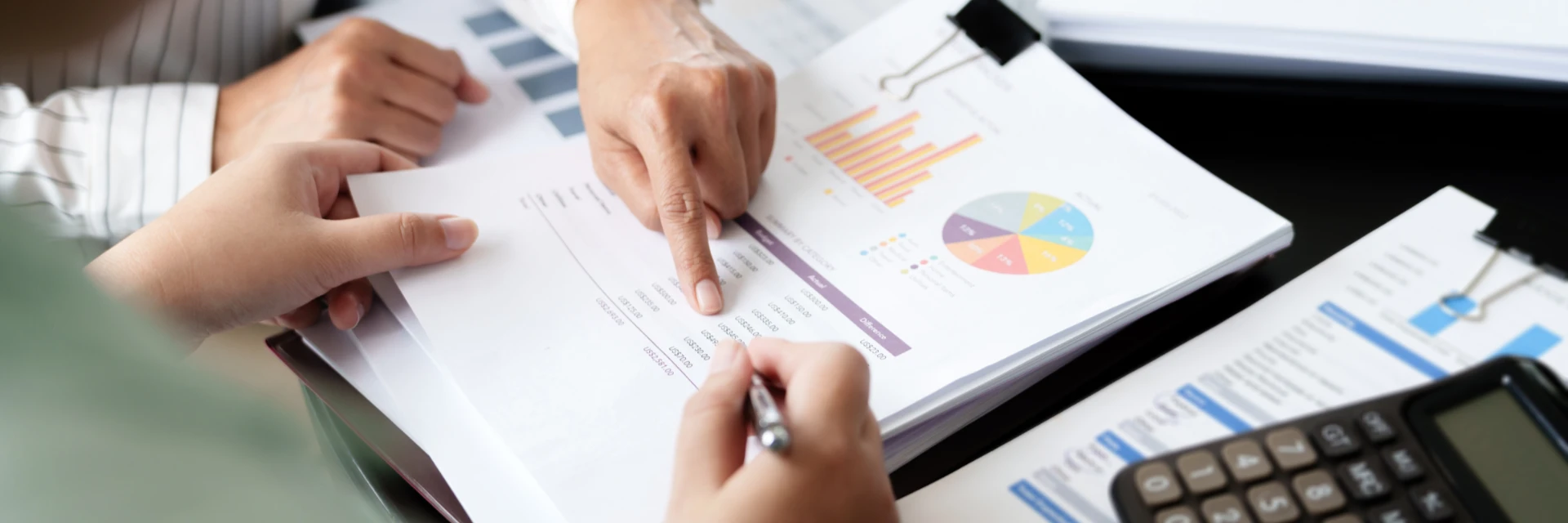 Deux mains analysant des rapports financiers avec des graphiques colorÃ©s et une calculatrice.