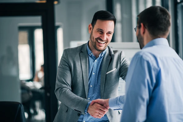 Deux hommes en chemise se sourient et se serrent la main chaleureusement dans un bureau.