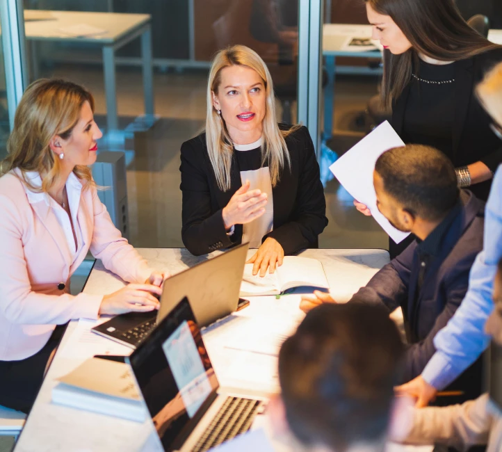 Une équipe échange autour d'une table de bureau avec ordinateurs et documents.