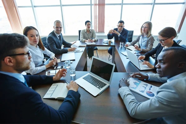 Un groupe diversifié collabore autour d'une grande table en U dans une salle de conférence.