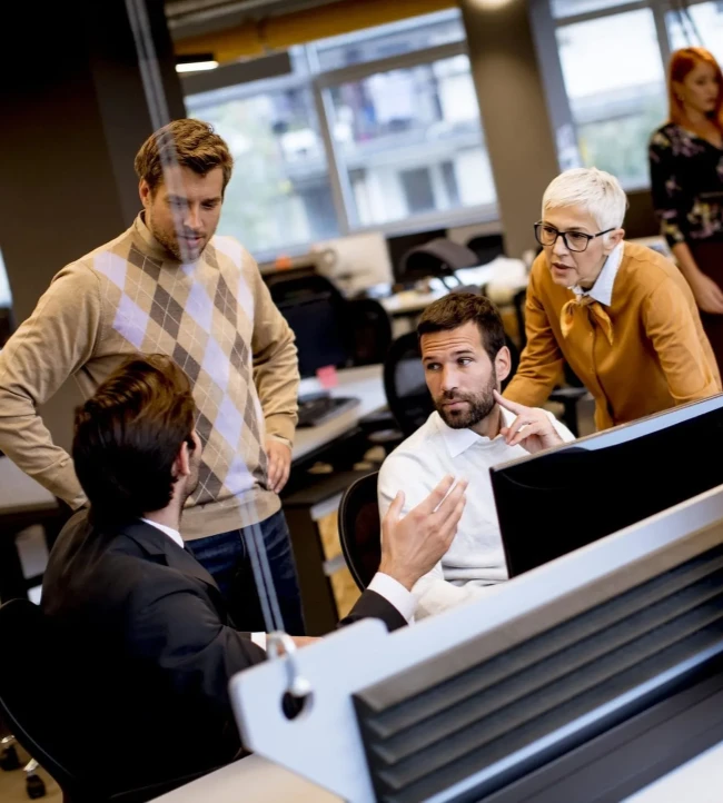 Collègues discutant dans un bureau moderne autour d'un ordinateur. Ambiance de travail active.